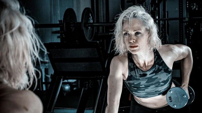 Ein älterer Mann beim Krafttraining in einem gut beleuchteten Fitnessstudio, konzentrierter und entschlossener Gesichtsausdruck, körperliche Vitalität als bewusste Lebensentscheidung