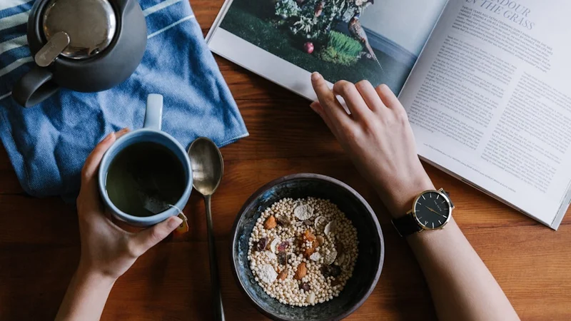 A desk with an open habit tracker journal, a pen, and a cup of coffee next to a small plant — morning light
