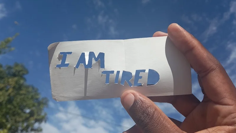 eine Person sitzt spät abends an ihrem Schreibtisch, die Hände auf der Tastatur, starrt auf einen leeren Bildschirm unter einer einzigen Schreibtischlampe — die Haltung von jemandem, der erschöpft, aber noch nicht fertig ist