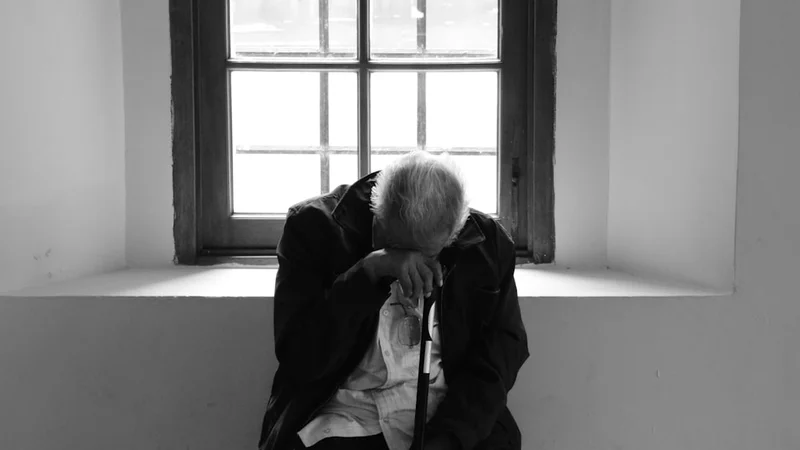 Eine ältere Person und ein junger Erwachsener sitzen sich in einer Küche gegenüber, Nachmittagslicht, beide halten Tassen