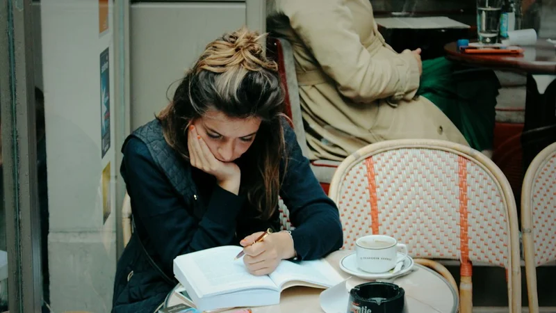 person writing in a small notebook at a café table, relaxed posture, coffee cup nearby, keyword: stress mindset journaling seven day experiment