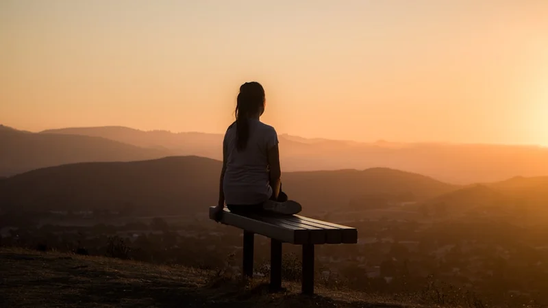 person seated cross-legged on a meditation cushion near a window with soft morning light, eyes closed, relaxed posture