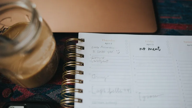 person sitting at a desk in early morning light writing in a habit tracking journal with a coffee cup beside them