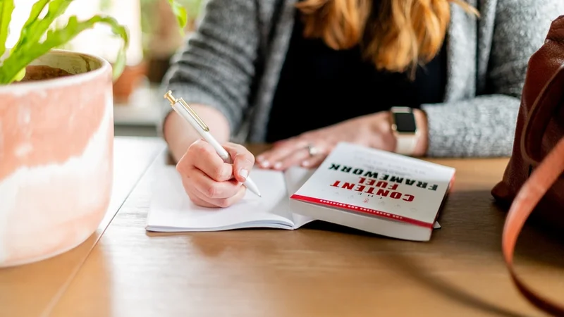 Persona escribiendo en un cuaderno en un escritorio con luz matinal entrando por la ventana, expresión tranquila y concentrada, taza de café abierta a su lado | construir confianza mediante la práctica deliberada y el diario personal