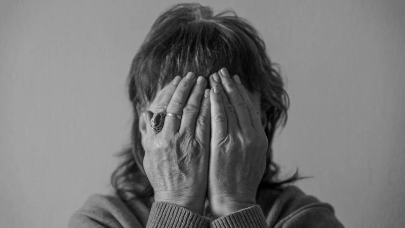 Una persona de unos cincuenta años sentada en un escritorio despejado rodeada de libros y un portátil, con expresión tranquila y concentrada, luz natural cálida desde la izquierda