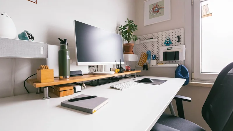 Vista cenital de una mesa organizada con un organizador de cajones etiquetado, cuaderno abierto, monitor en brazo articulado y superficie de trabajo despejada