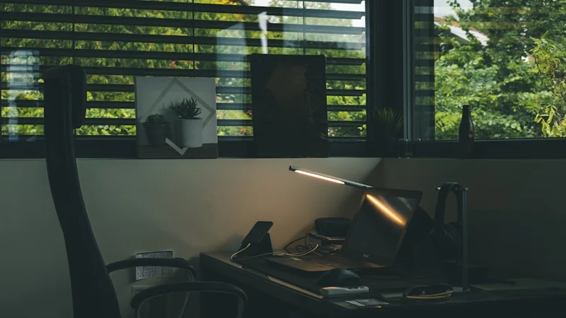 persona sentada sola en un escritorio de oficina poco iluminado, mirando una silla vacía frente a ella, con expresión insegura