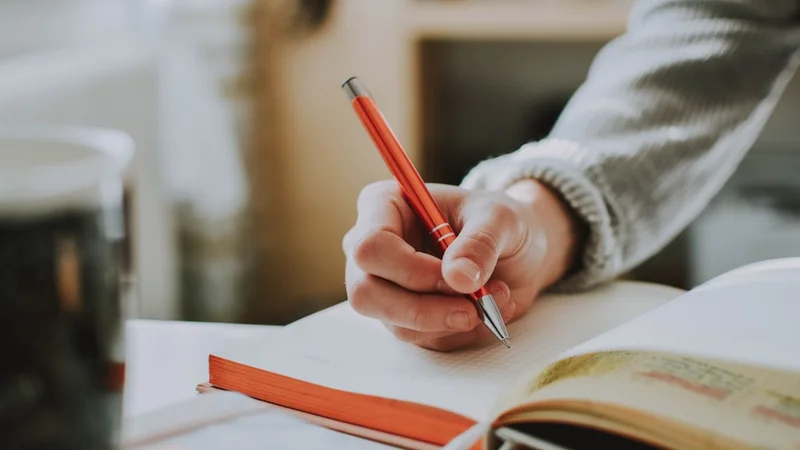 Una persona escribiendo en un diario en un escritorio con una bebida caliente cerca, revisando pensativamente su actuación