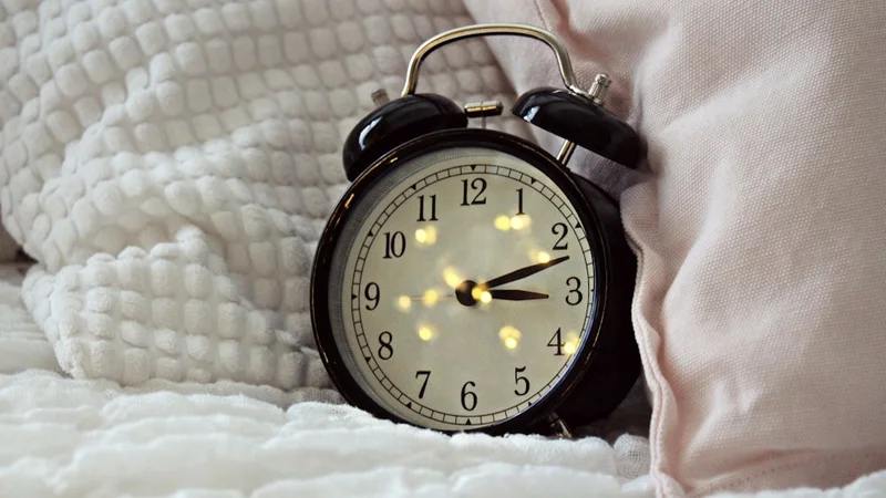 personne assise dans son lit à l'aube, lumière solaire entrant par la fenêtre, l'air reposé et alerte