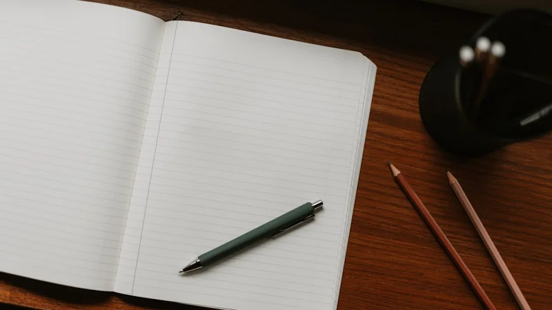 Personne écrivant dans un journal privé à la lumière d'une lampe tôt le matin, carnet ouvert sur un bureau en bois
