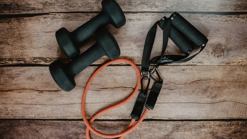 setup minimale per l'allenamento con scarpe da corsa, un elastico di resistenza e un piccolo quaderno su un pavimento in legno