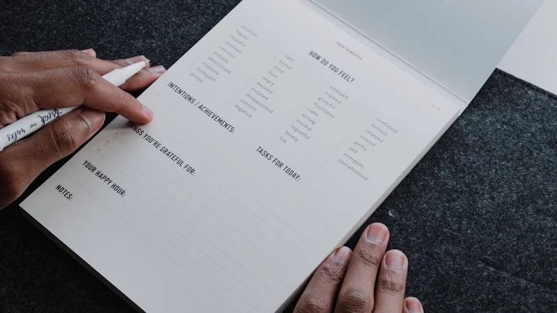 Um diário aberto e minimalista com o cabeçalho «Lista de coisas para parar de fazer» escrito à mão e três itens riscados sobre uma mesa organizada