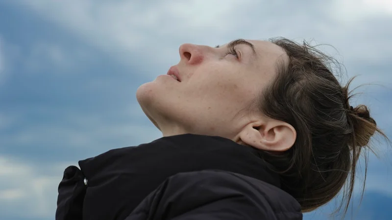 Pessoa sentada com os olhos fechados praticando respiração consciente, luz suave da manhã filtrando por uma janela, postura relaxada